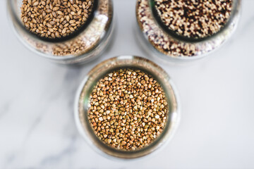 healthy whole grains and legumes in clear pantry jars on marble background including quinoa buckwheat and barley,, simple ingredients concept