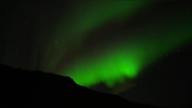 Cinematic shot of Green Northern Lights and stars at sky during dark night between mountains and volcano of Iceland