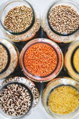 red lentils and other healthy whole grains and legumes in clear pantry jars on marble background,...