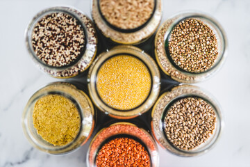 polenta cornmeal and other healthy whole grains and legumes in clear pantry jars on marble background, simple ingredients concept
