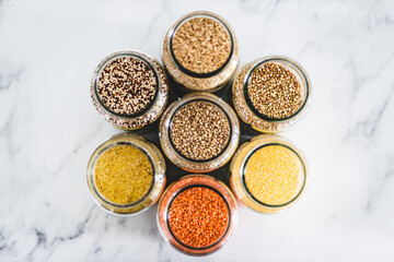 barley and other healthy whole grains and legumes in clear pantry jars on marble background, simple ingredients concept
