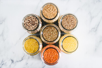 buckwheat and other healthy whole grains and legumes in clear pantry jars on marble background, simple ingredients concept