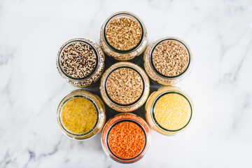 brown rice and other healthy whole grains and legumes in clear pantry jars on marble background,...
