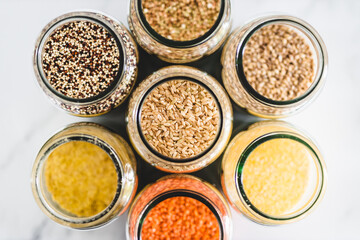 Fototapeta na wymiar brown rice and other healthy whole grains and legumes in clear pantry jars on marble background, simple ingredients concept