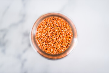 red lentils in clear pantry jar on marble background, simple ingredients concept