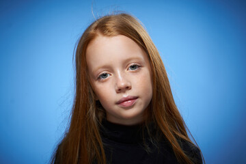 redhead girl with freckles on her face posing close-up blue background