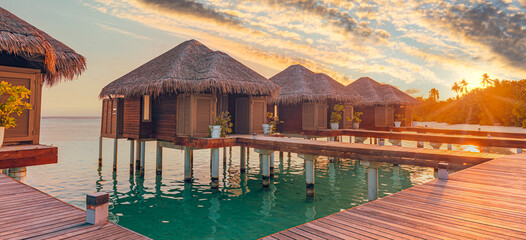 Sunset on Maldives island, luxury water villas resort hotel and wooden pier. Colorful sky and...