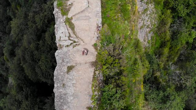 Aerial: zenital shot of a man with a suitcase walking on a clif