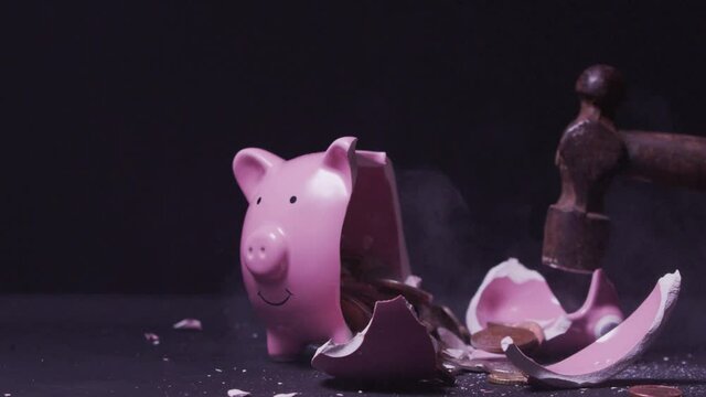 Breaking a pink piggy bank full of coins money with a hammer over black background