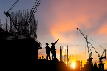 Silhouette of Engineer and worker on building site, construction site at sunset in evening time.