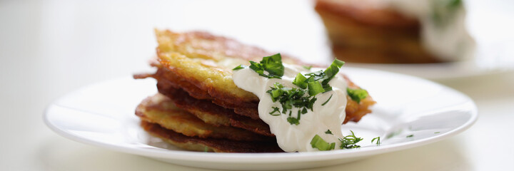 Potato pancakes with sour cream and herbs on white plate closeup