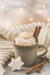 Cup of coffee or hot chocolate with cream, cinnamon and cookie, fairy light in the background, vertical with copy space