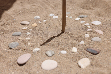 Wooden stick and pebbles on sand showing time by shadow © H_Ko