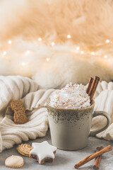 Obraz na płótnie Canvas Gray cup of coffee or hot chocolate with cream, cinnamon and cookie, fairy light in the background, vertical with copy space