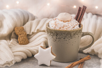 Cup of coffee or hot chocolate with cream, cinnamon and christmas cookies, fairy lights in the background