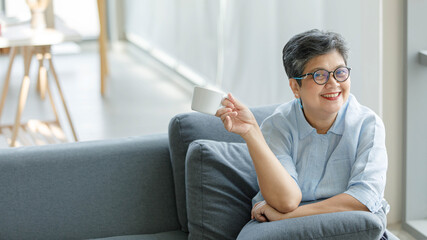 Merry Asian woman enjoying hot drink on sofa