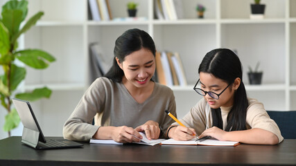 Happy asian mother helping her daughter doing homework.