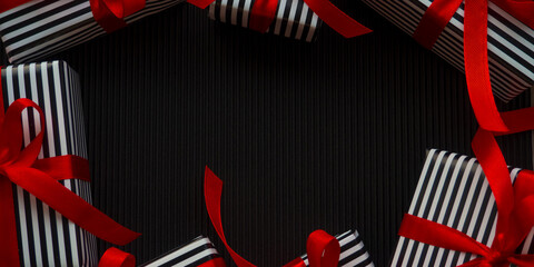 Gifts on the black background. Small gifts in a stripped black and white wrapper and with red ribbons on the dark corrugated cardboard. Christmas sale shopping. Black Friday and Cyber Monday.