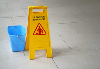 Cleaning in progress yellow sign with blue bucket on the pavement, Wet floor caution sign