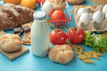 Set of fresh products and a miniature shopping cart on a blue background top view. Online shopping concept, food delivery