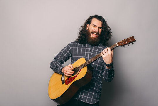 Photo of young man with long hair and beard paying at acoustic guitar.