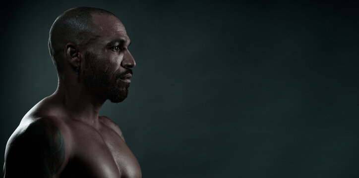 Studio portrait of African man in profile on dark background. Strong and muscular Cuban with naked torso. Side view. advertising banner or flyer for ad