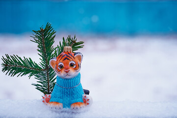 Tiger cub with Christmas tree toy outdoors. Snowflakes are falling. Blurred background. The symbol of the new year 2022.