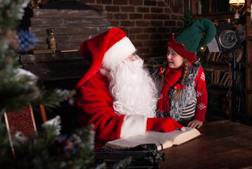Santa Claus and elf with a sweet smile whispers Santa Claus in his ear sitting at a huge wooden table for the New Year and Christmas 2022