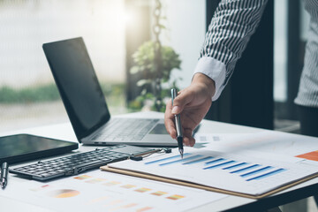 Businessman holding pen and pointing paper chart summary analyzing annual business report with using laptop at room office desk.