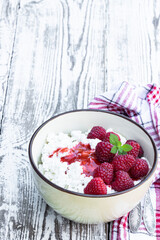 Cottage cheese with raspberry in ceramic bowl on white wooden table