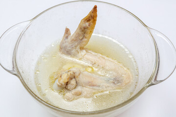 Boiled chicken wing lies in a deep glass bowl with chicken broth.