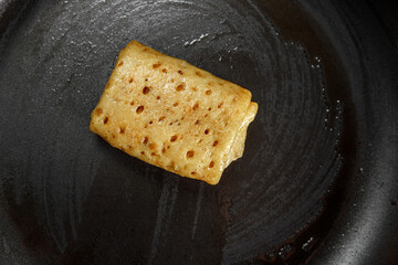The stuffed pancake lies in a frying pan, with a non-stick coating, greased with oil.
