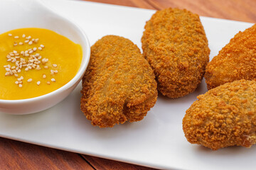 Traditional spanish snack- croquettes fried in oil, with yellow sauce on white plate. Side view on wooden background.