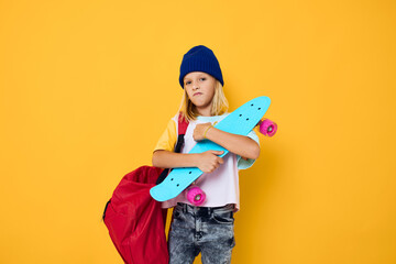 Charming little blonde kid girl with a skateboard on his head yellow background