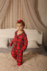 a beautiful little girl in Christmas pajamas red in a cage is standing on the bed