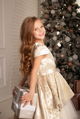 charming little girl 8 years old for the holiday New Year and Christmas 2022 holds a gift of silver color behind her