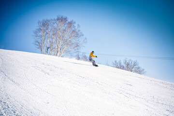 Snowboarder riding down the hill in front of blue sky