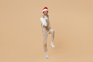 Fototapeta na wymiar Full body overjoyed excited young african man 20s in Santa Claus red Christmas hat do winner gesture isolated on plain pastel beige background studio portrait. Happy New Year 2022 celebration concept.