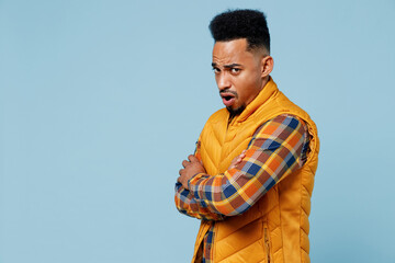 Side profile view perplexed concerned young black man 20s years old wears yellow waistcoat shirt look camera hold hands crossed yawning isolated on plain pastel light blue background studio portrait.