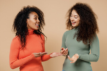 Two excited laughing young curly black women friends 20s wearing casual shirts clothes look at each...