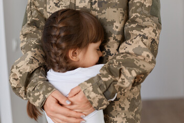 Portrait of faceless military woman wearing camouflage uniform hugging her little cute daughter, mother missing her kid very much while being in army.