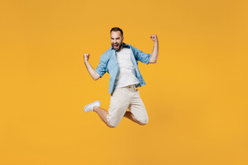 Fototapeta na wymiar Full body young overjoyed satisfied happy caucasian man 20s wearing blue shirt do winner gesture clench fist jump high isolated on plain yellow background studio portrait. People lifestyle concept