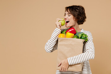 Young smiling vegetarian caucasian woman 20s in casual clothes hold paper bag with vegetables...