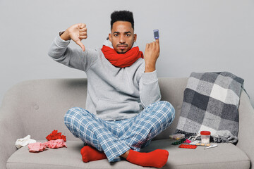 Young african man in grey sweater scarf sit sofa use pulse oximeter checking saturation show thumb...