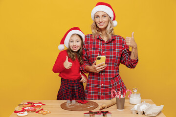 Two woman mother fun child baby girl in red Christmas hat isolated on plain yellow wall background studio. Mom little kid cook ginger cookie at kitchen table home. Happy New Year 2022 holiday concept