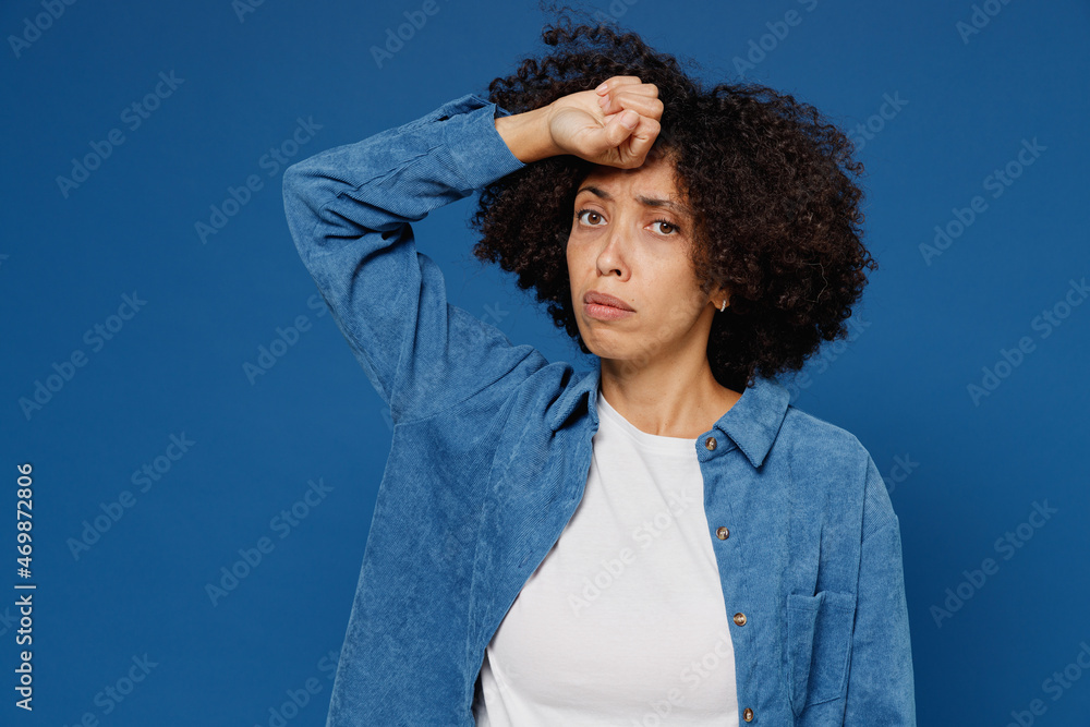 Wall mural Young sick tired exhausted ailing black woman in casual clothes shirt white t-shirt put hand on forehead have headache isolated on plain dark blue background studio portrait. People lifestyle concept.