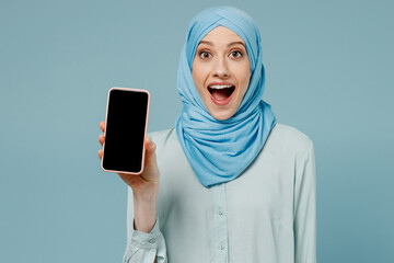 Young arabian asian muslim woman in abaya hijab hold in hand use mobile cell phone with blank screen workspace area isolated on plain blue background People uae middle eastern islam religious concept