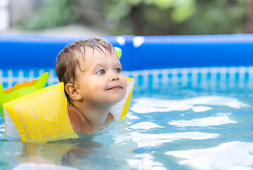 Fototapeta na wymiar Kid in oversleeves swims in the pool in the yard