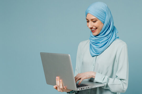 Young Smiling Happy Arabian Asian Muslim Woman In Abaya Hijab Hold Use Work On Laptop Pc Computer Isolated On Plain Blue Background Studio Portrait. People Uae Middle Eastern Islam Religious Concept.