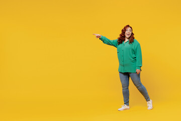 Fototapeta na wymiar Full size body length excited happy vivid young ginger chubby overweight woman 20s wears green shirt go point on workspace area copy space mock up isolated on plain yellow background studio portrait.